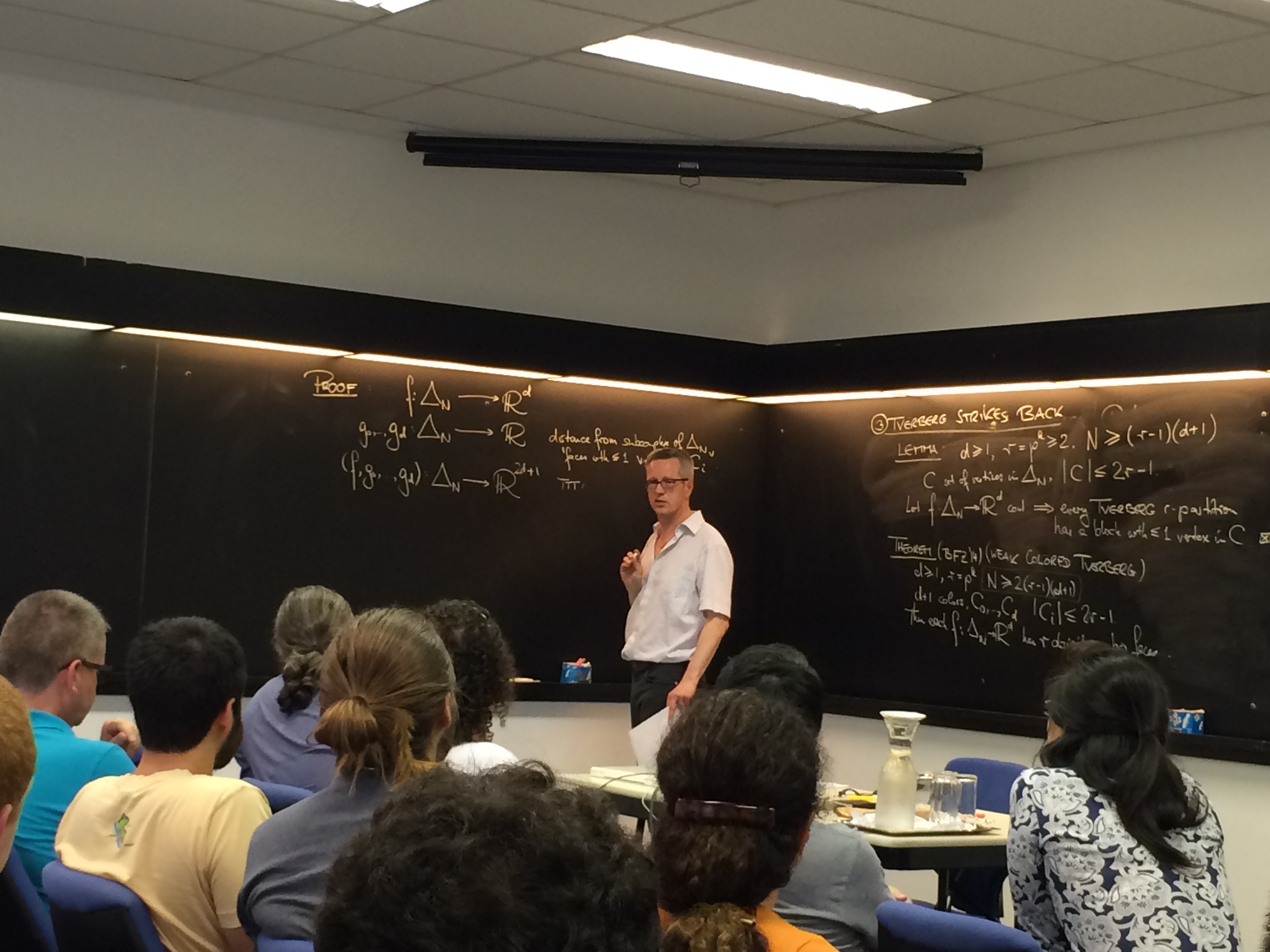 Professor Ziegler vor einer großen Tafel mit mehreren mathematischen Formeln stellt seine Lecture dem Publikum vor