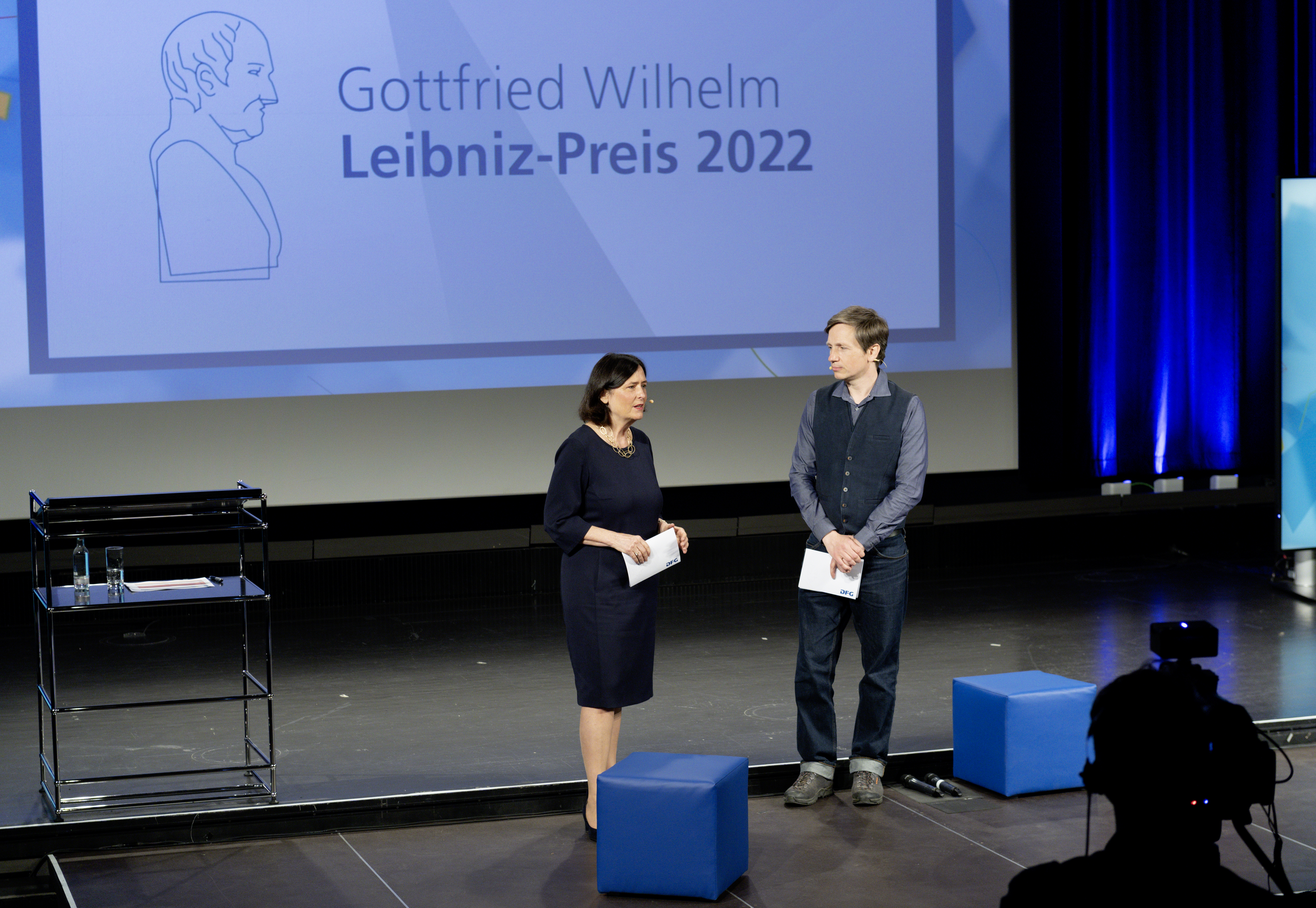 DFG-Präsidentin Katja Becker begrüßt die geladenen Gäste sowie die Zuschauerinnen und Zuschauer des Livestreams gemeinsam mit Moderator Johannes Büchs.