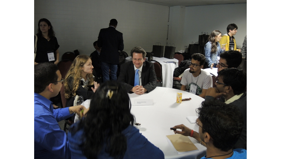 A imagem mostra diversas pessoas sentadas à mesa, com o Prof. Koch ao centro