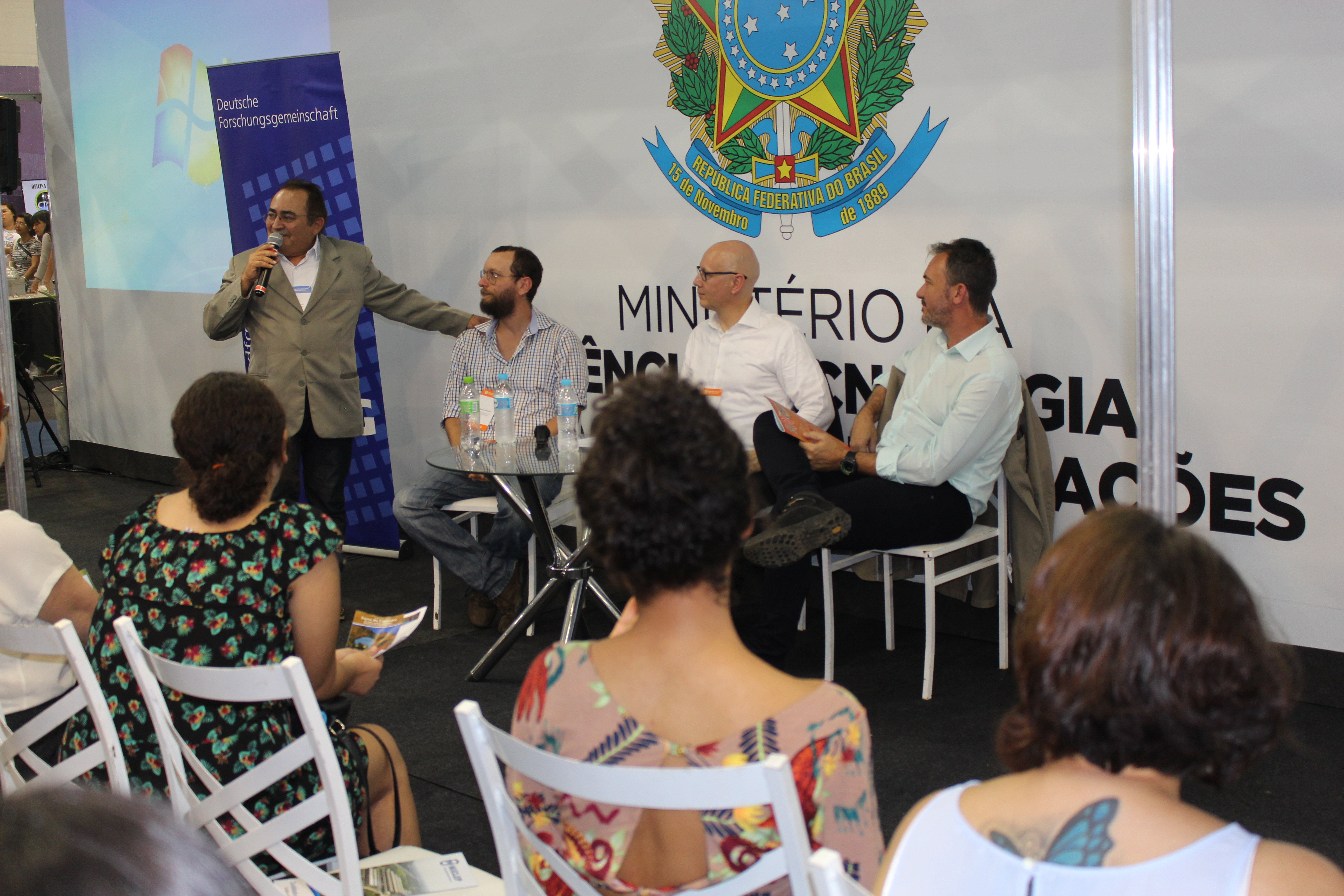 Francisco Guedes em pé ao lado dos participantes da mesa-redonda (sentados) diante do público