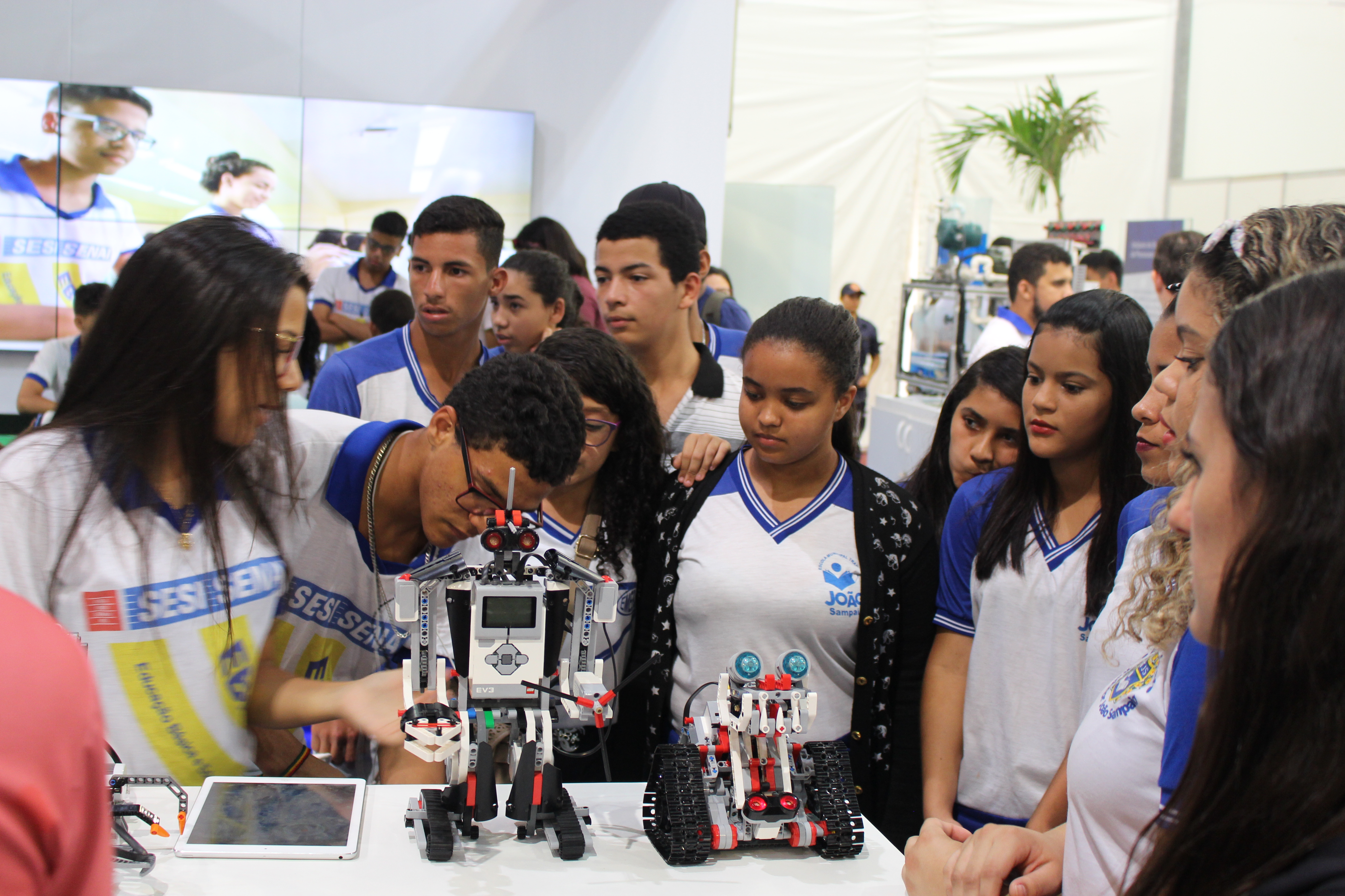 Grupo de jovens com uniformes escolares divertem-se com robô em exposição