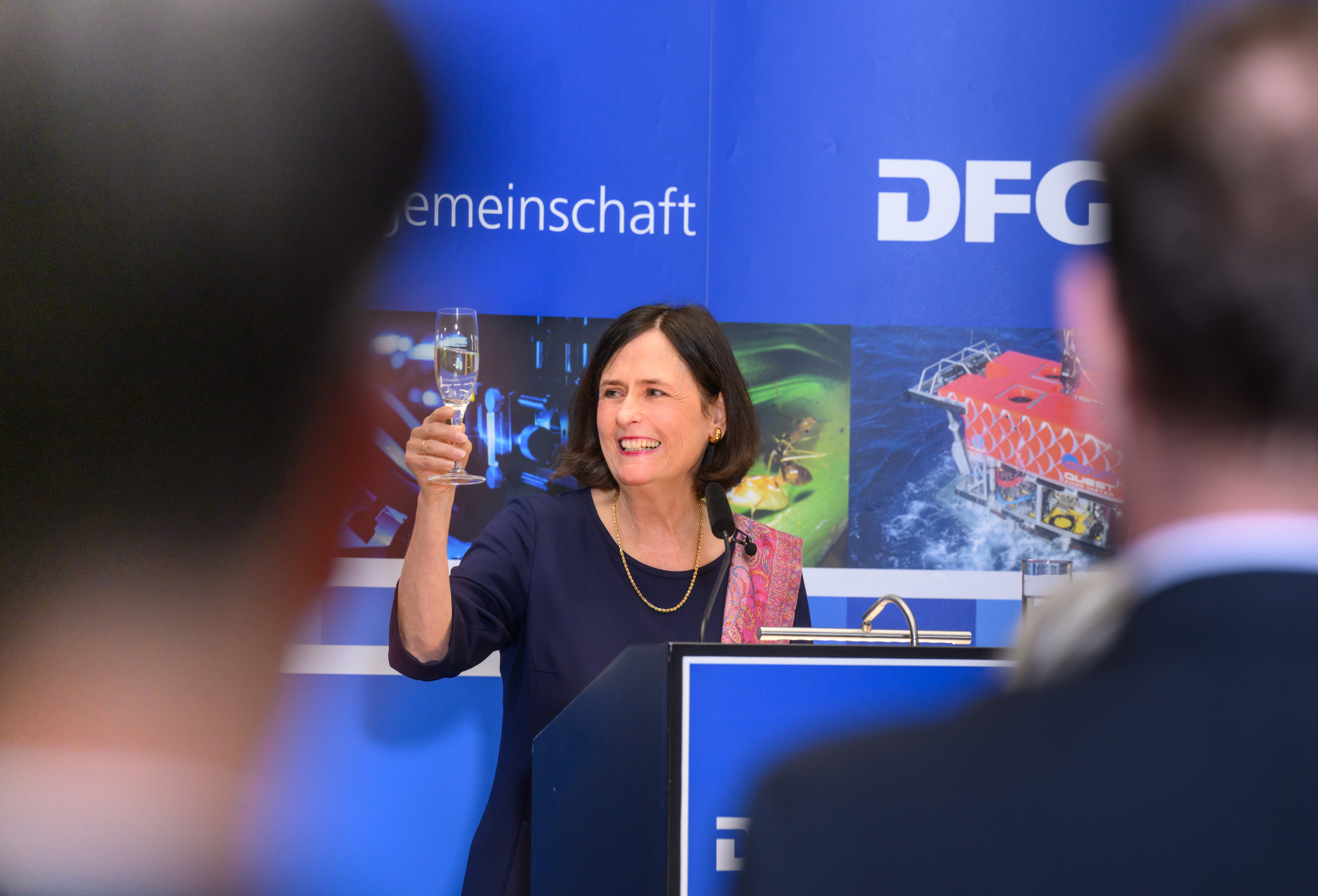 DFG-Präsidentin Prof. Dr. Katja Becker hebt zum Ende ihrer Rede am Pult ein Sektglas