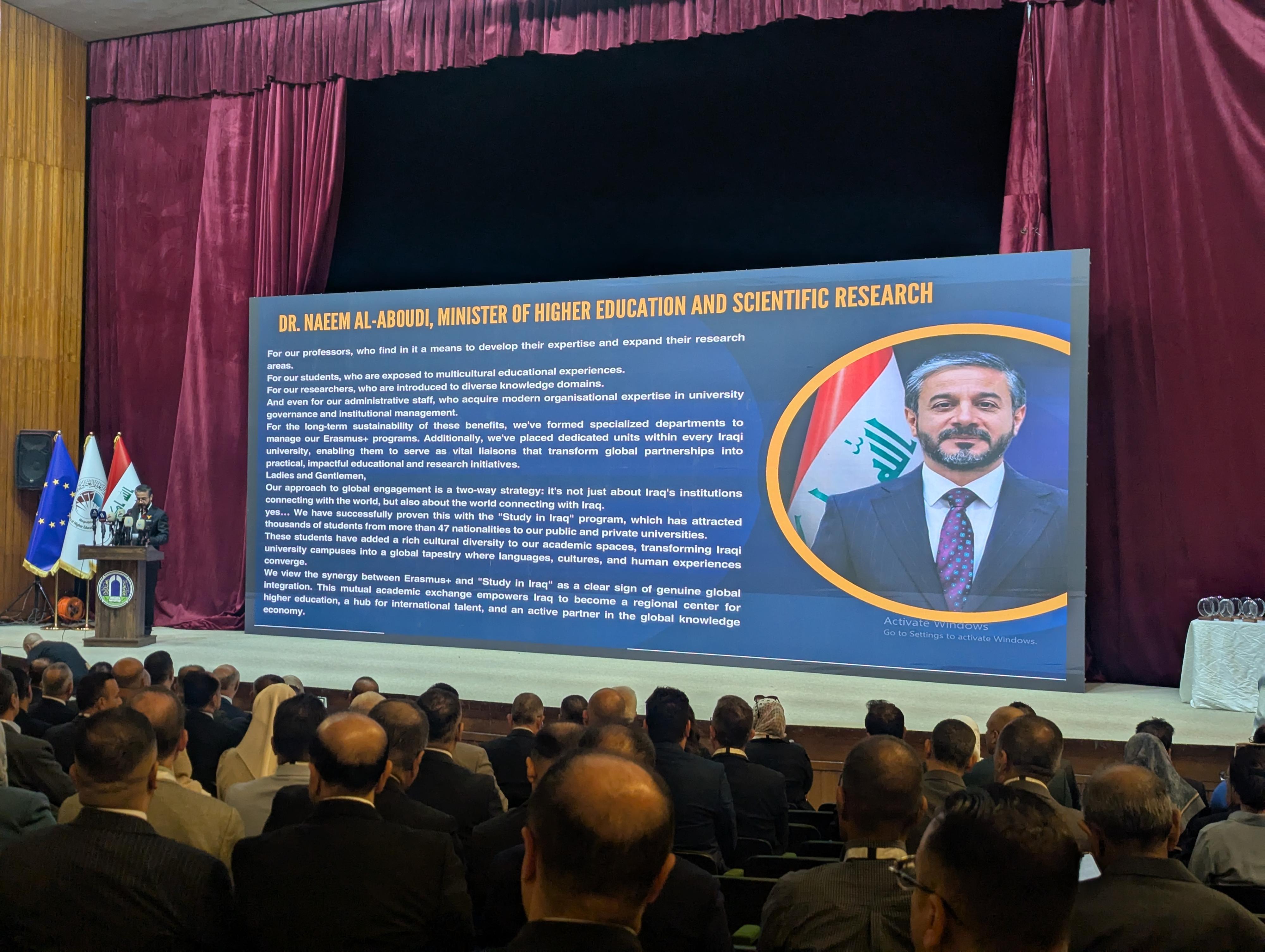 Der Minister steht am Rednerpult, daneben ist eine große Leinwand mit Informationen zu seiner Person zu sehen.