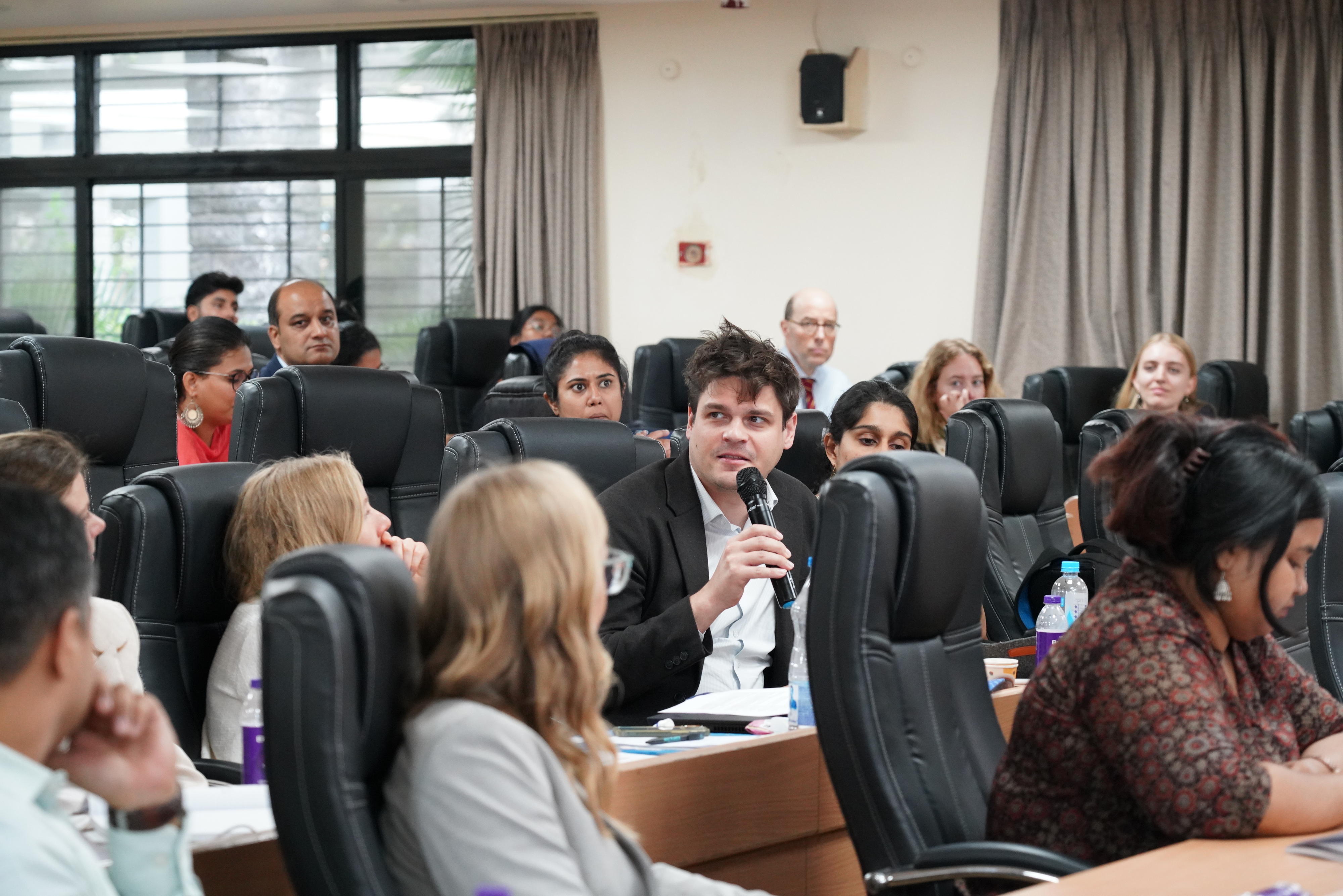 One participant is speaking while other participants look at him or take notes.