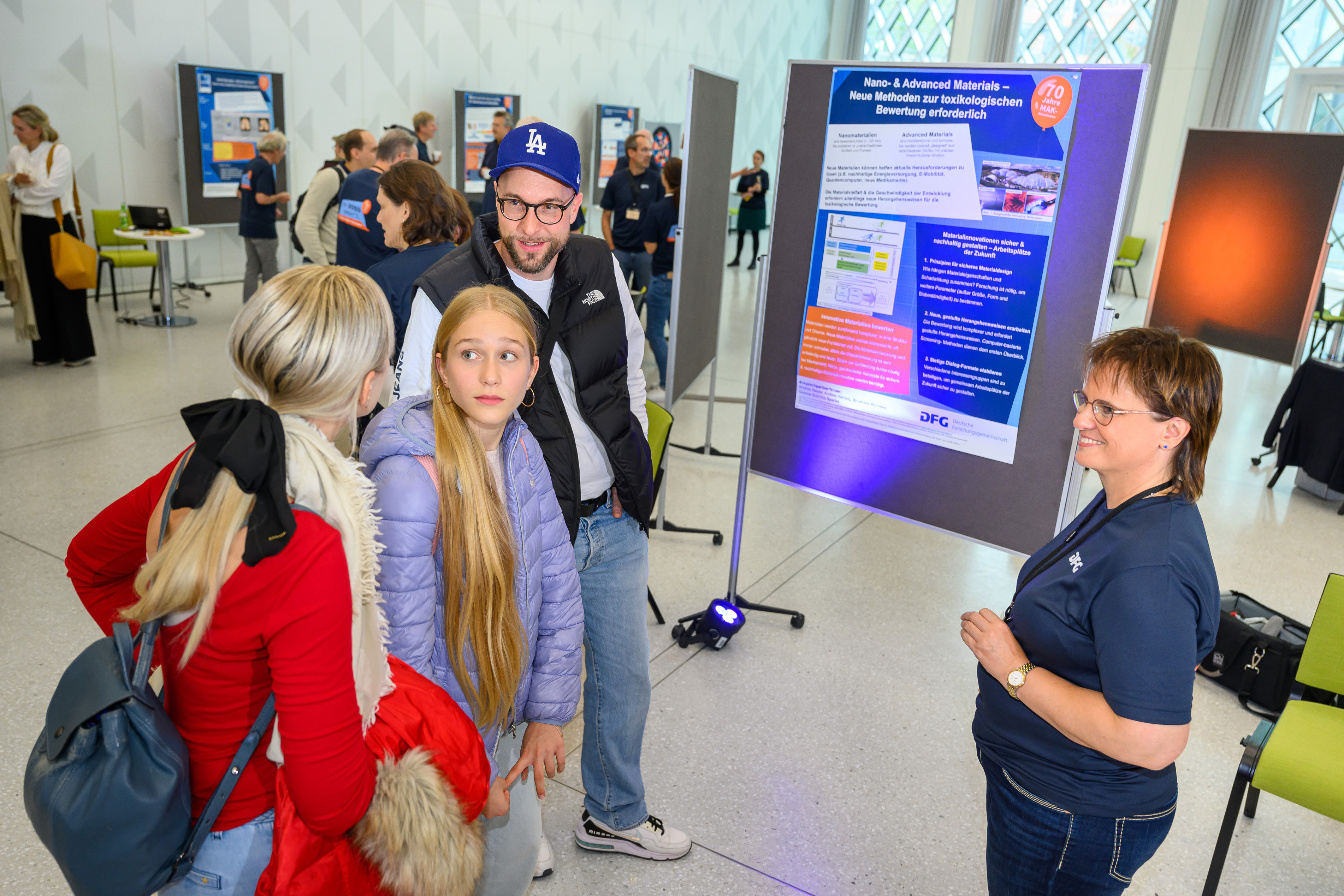 Eine dreiköpfige Familie ist an einem Poster im Gespräch mit einer Expertin
