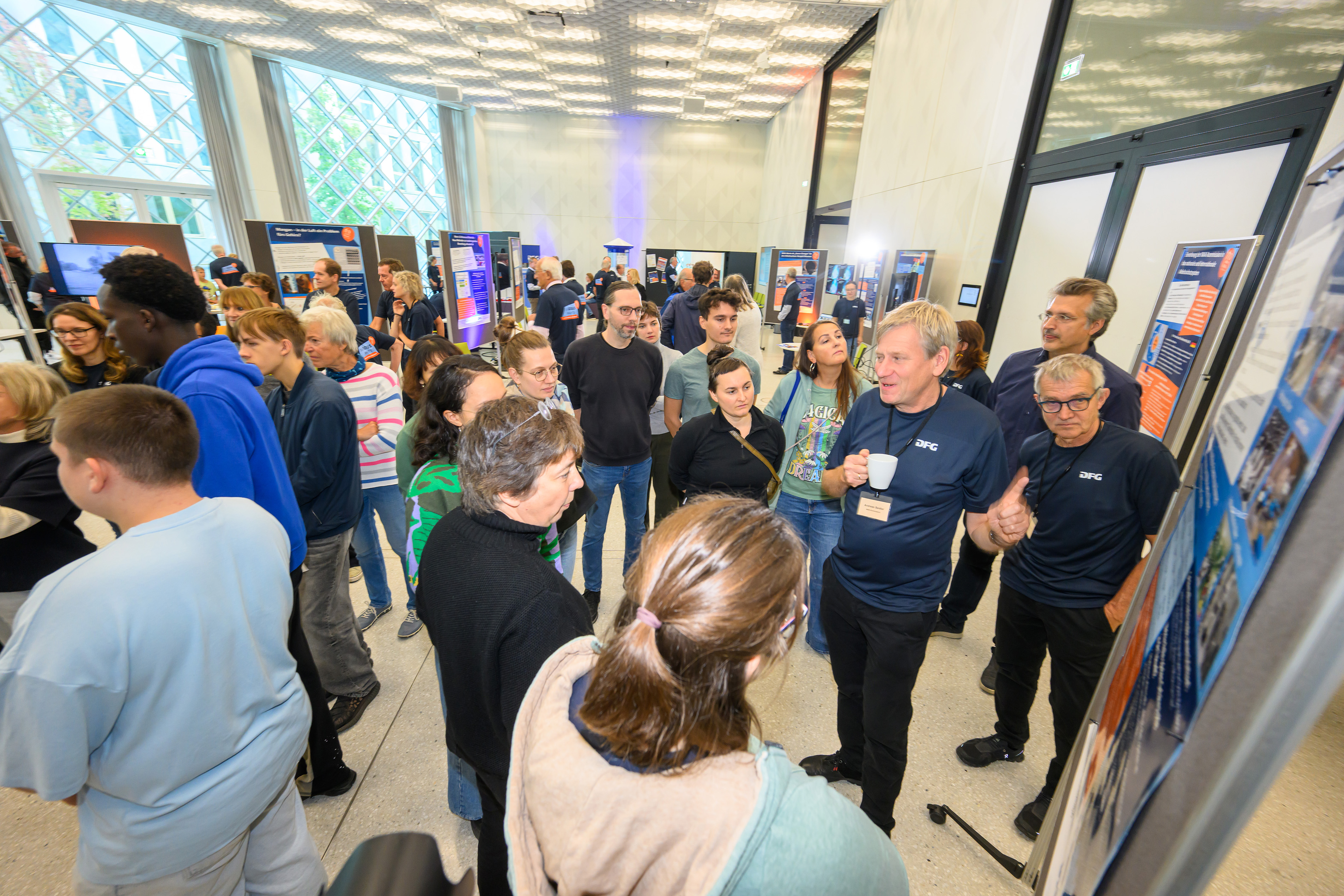 Ein Experte steht vor einem Poster und spricht zu einer Gruppe von Besucher*innen 