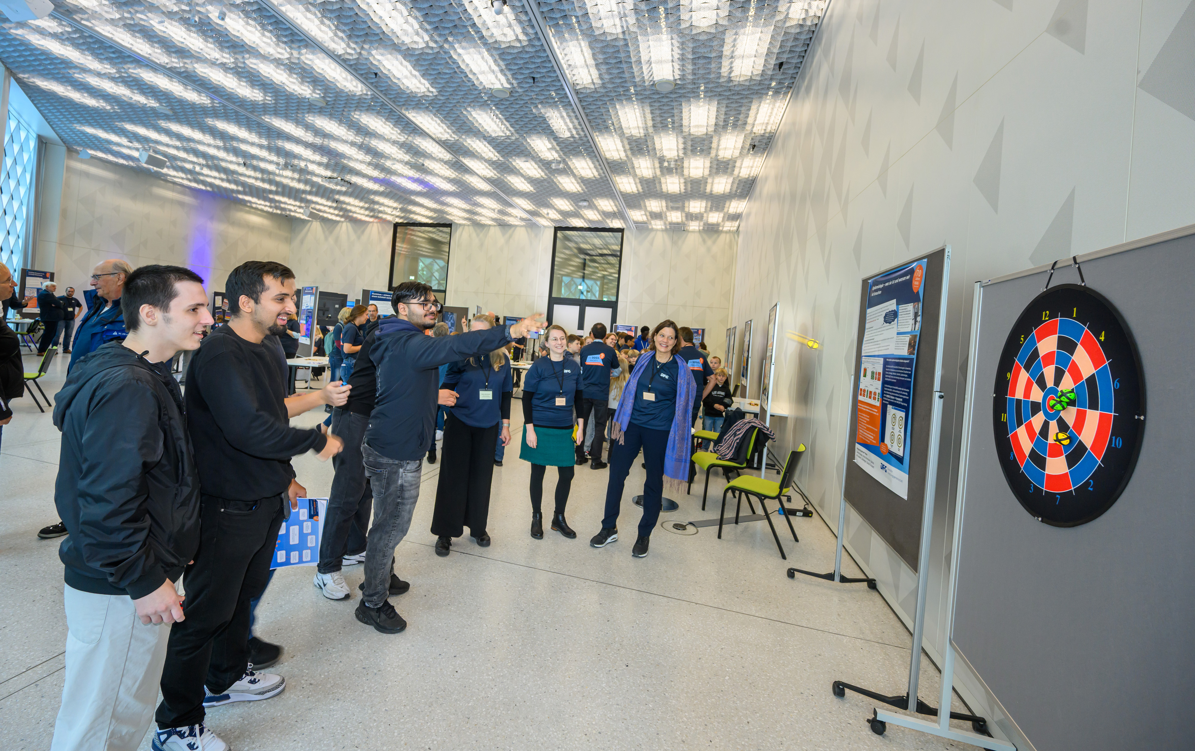 Zwei junge Männer stehen vor einer Dartscheibe und einer versucht, die Mitte zu treffen.