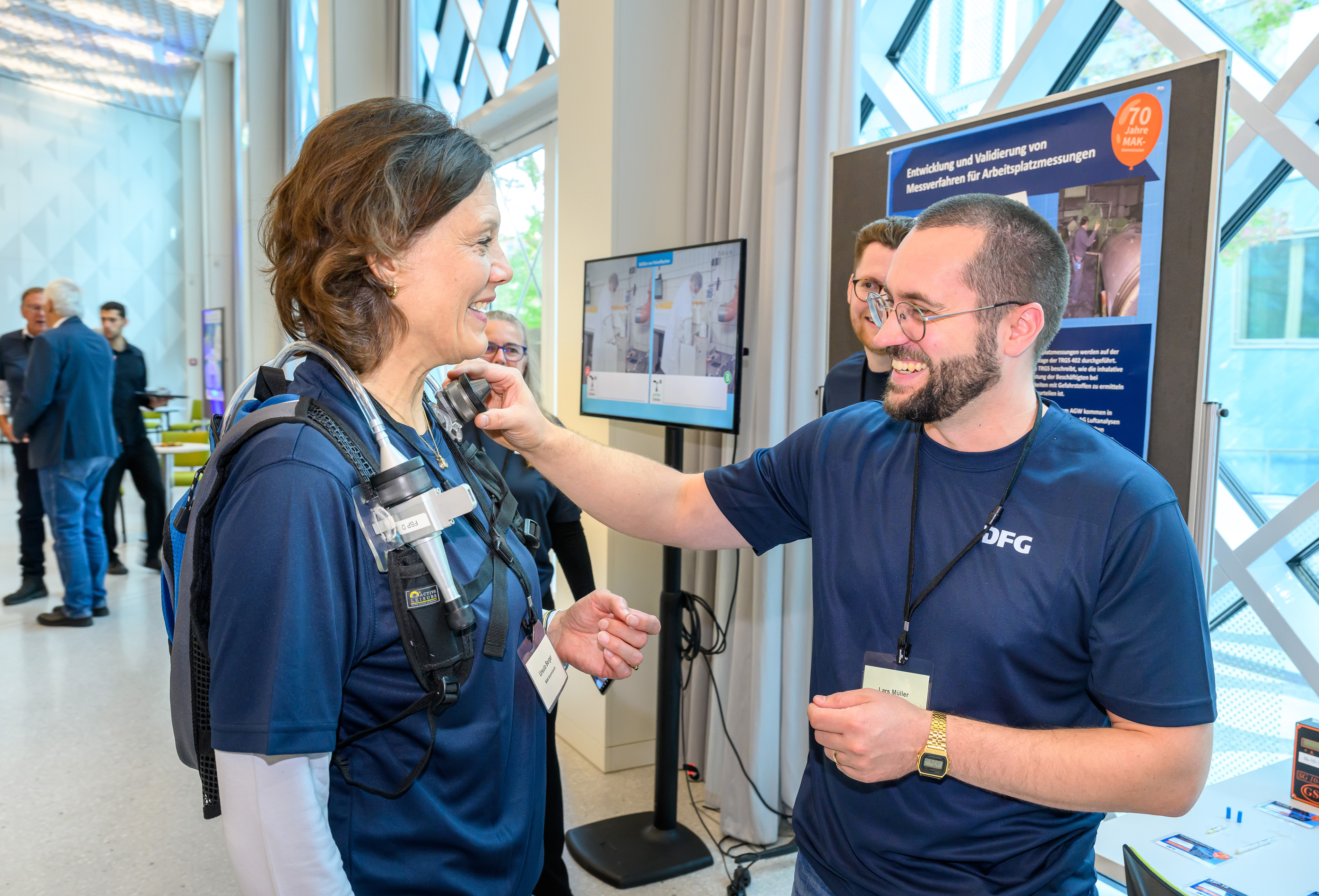 Eine Person legt einer anderen ein messgerät an, dass den Oberkörper umschließt. beide lächeln und sprechen miteinander