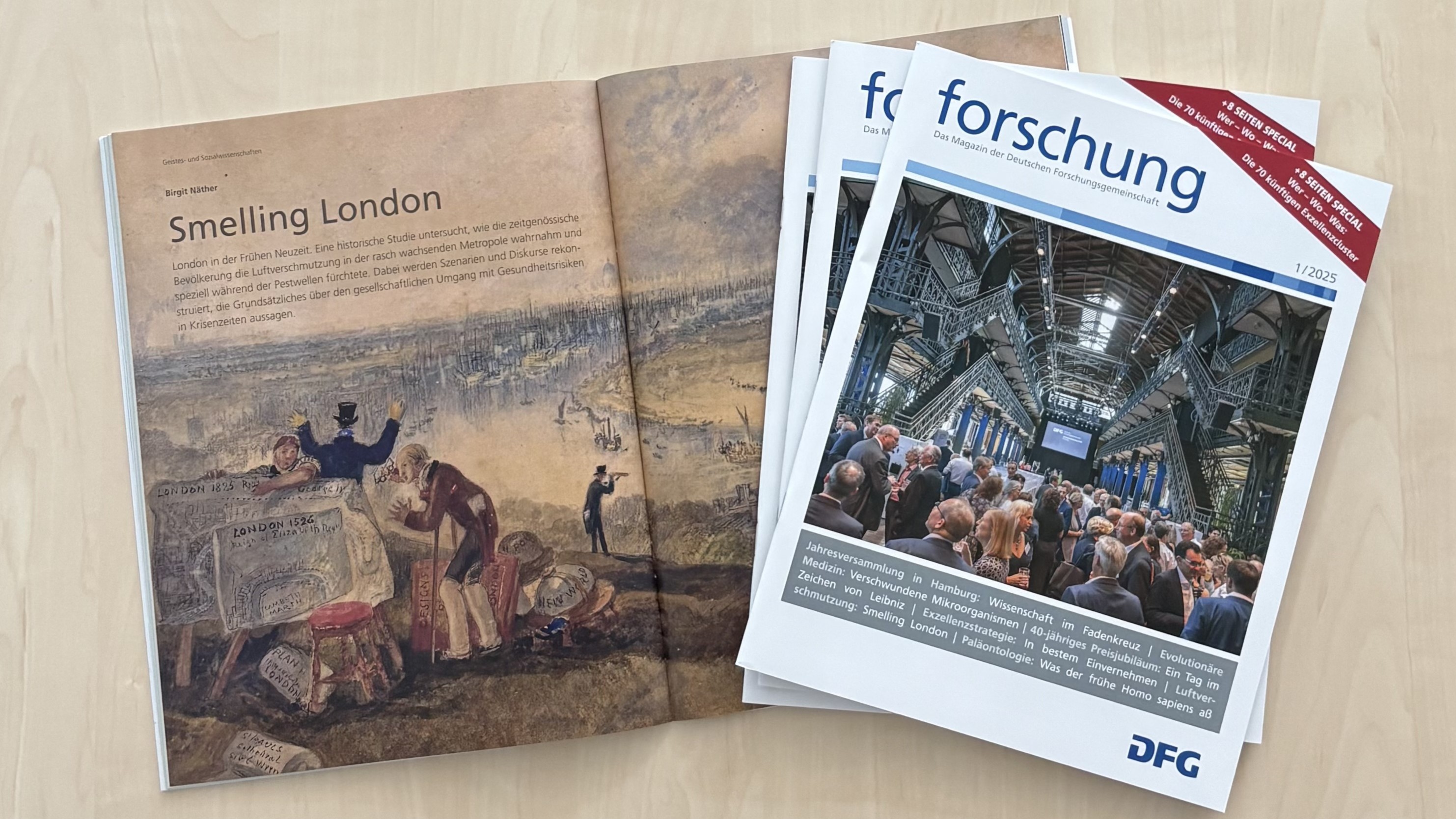 An open and two closed issues of "forschung" laying on a wooden table.