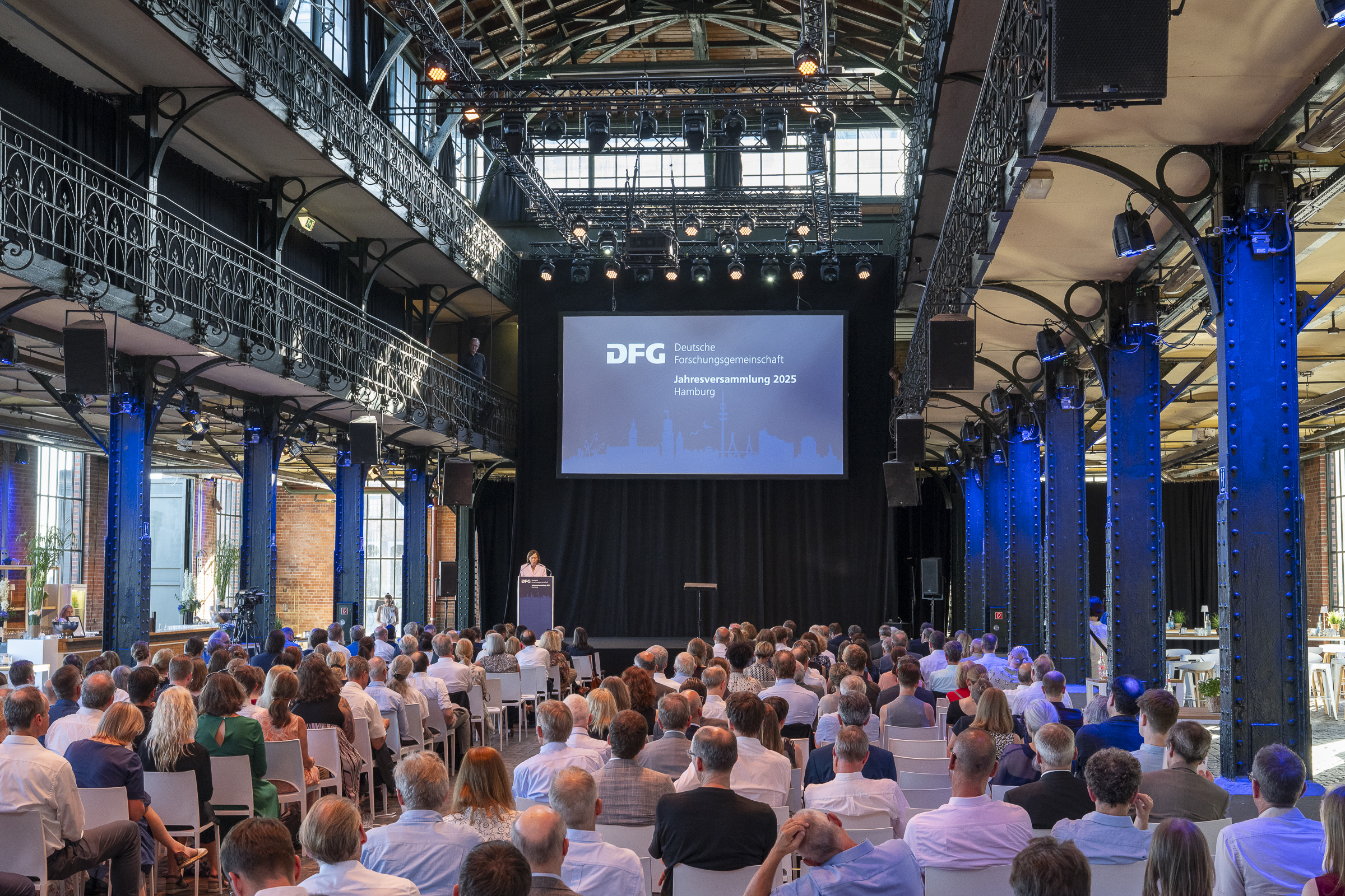 View into the hall with participants of the Annual Meeting 2025. In the background, there is a screen with DFG slides.