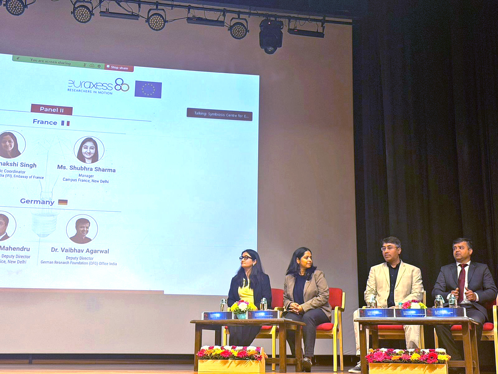 picture of the speaker's podium with the following speakers, from left to right: Shubhra Sharma, Manager at Campus France New Delhi; Dr. Meenakshi Singh, Scientific Coordinator, French Institute in India (IFI), Embassy of France; Mr. Apoorv Mahendru, Director Marketing & Deputy Director, DAAD Regional Office New Delhi, Dr. Vaibhav Agarwal, Deputy Director, Deutsche Forschungsgemeinschaft DFG Office India