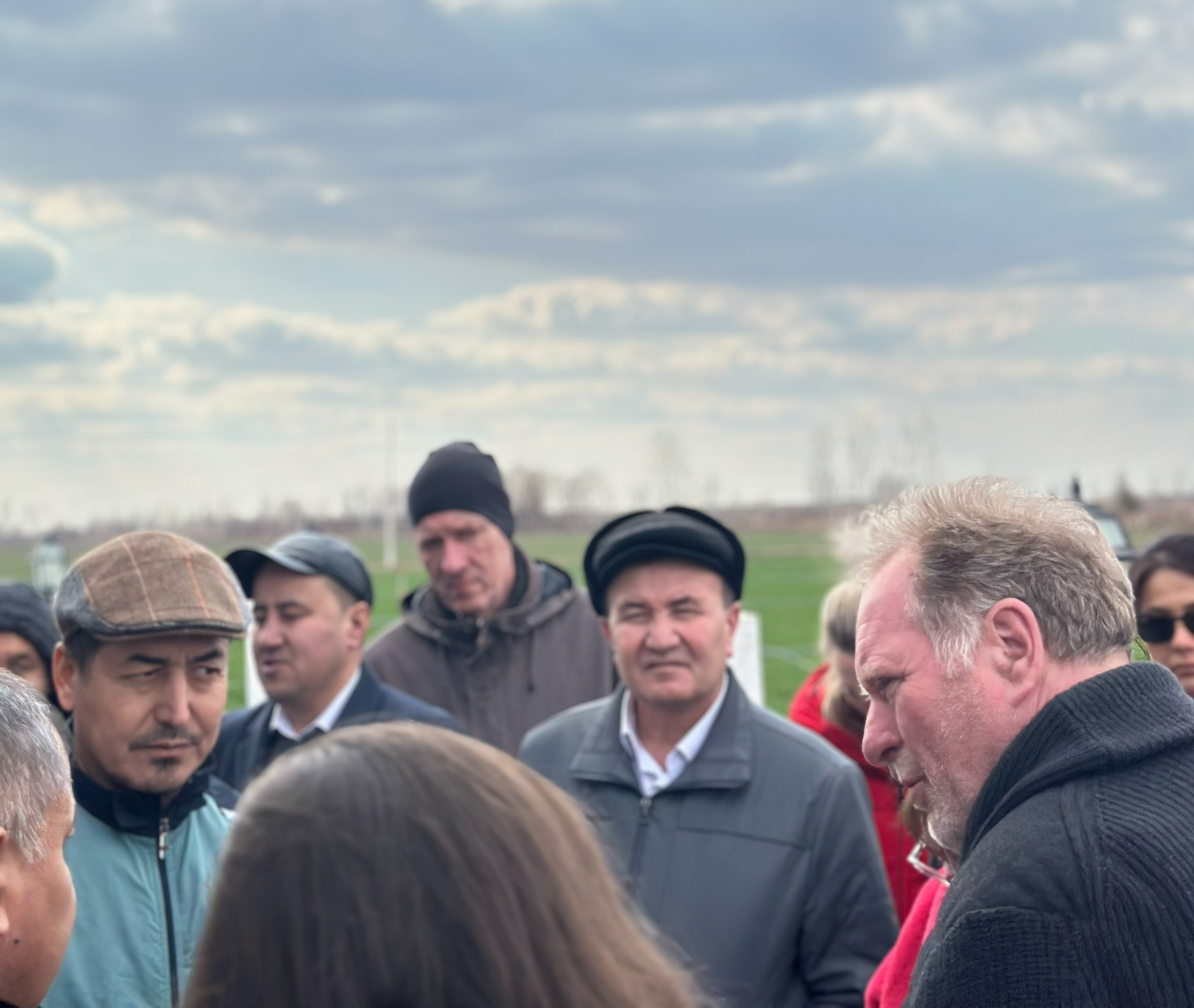 group picture of workshop participants talk to a farmer cooperating with Urgench State University about “precision management” in fruit and vegetable cultivation.