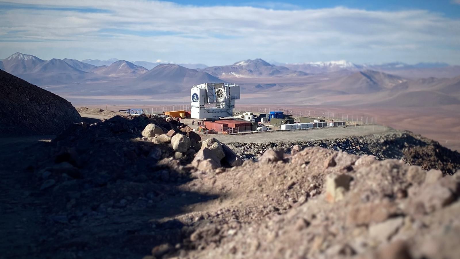Another view of the Fred Young Submillimeter Telescope on a plateau surrounded by mountains in the background.