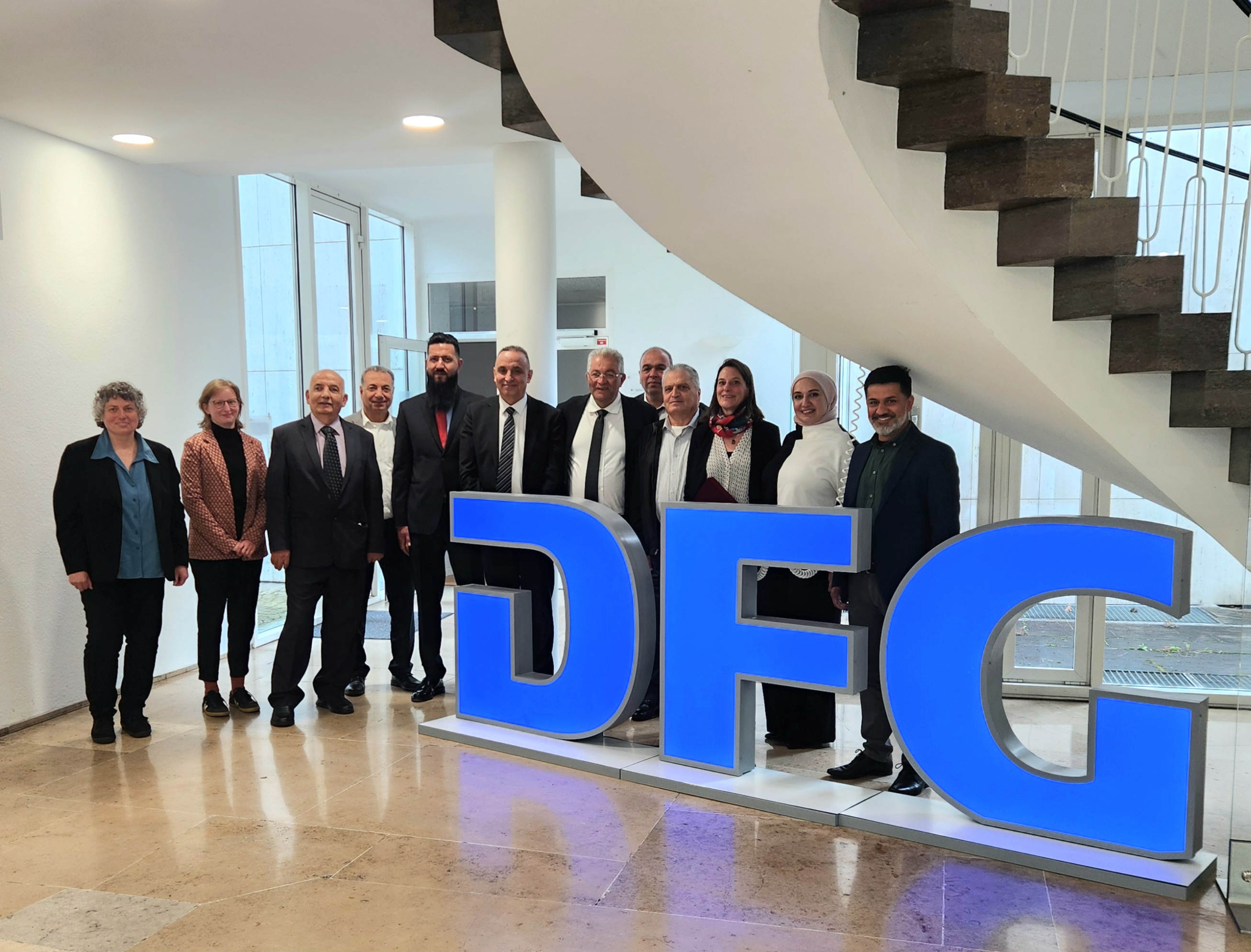 Vertreter*innen von DFG und der Delegation der Al-Quds-Universität posieren neben dem DFG-Zeichen.