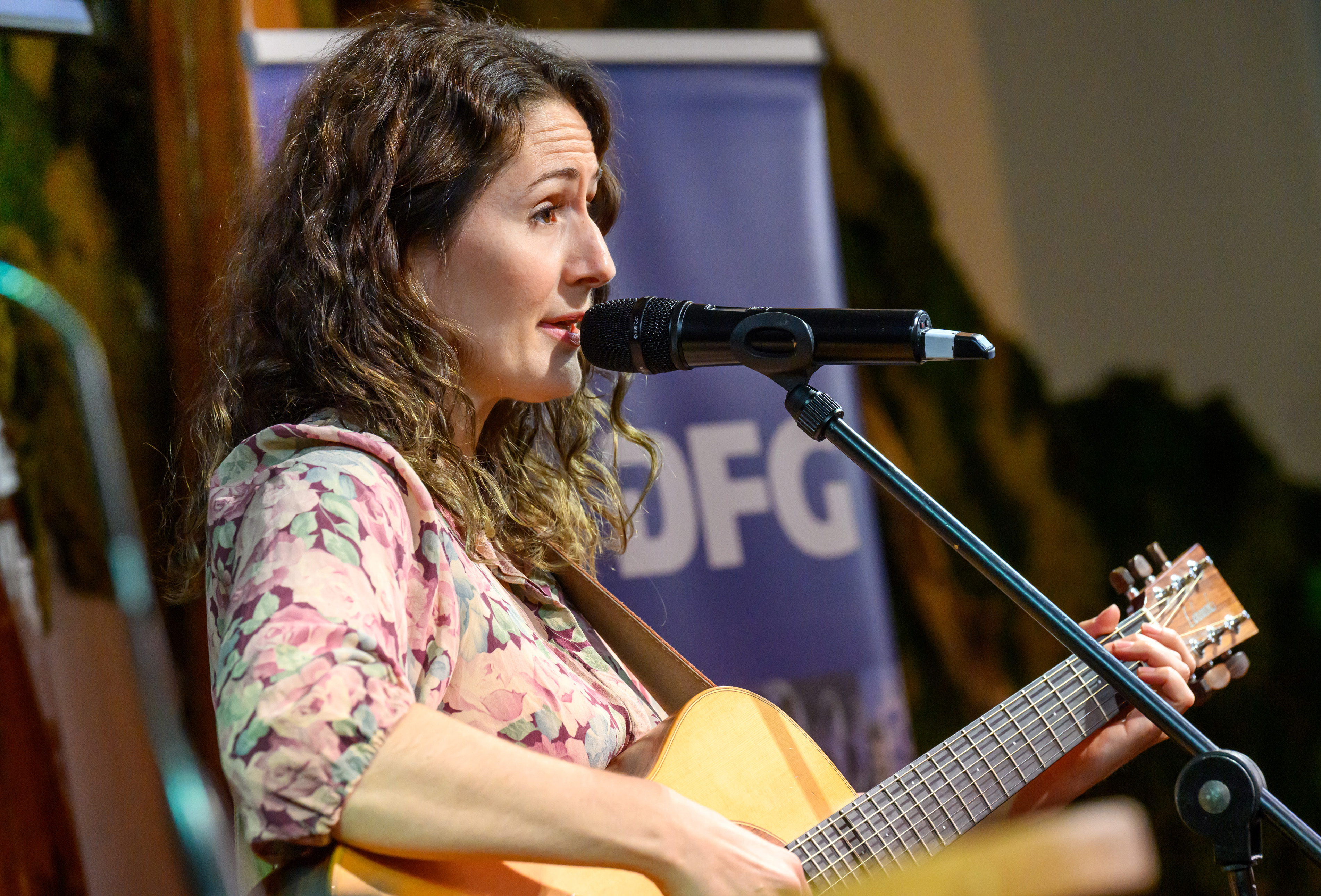 Bild der Sängerin und Songwriterin Lena Minder. Sie sitzt mit einer Gitarre vor einem Mikrophon und singt