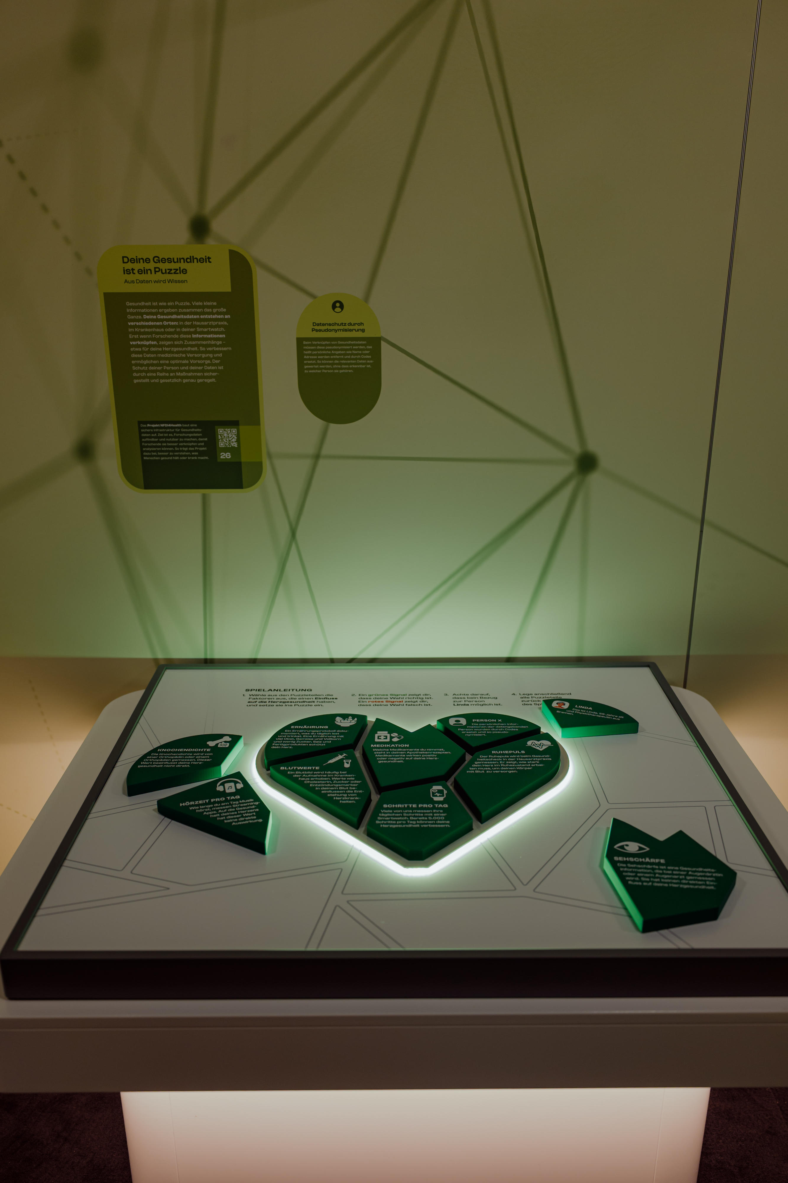 Ausstellungstisch mit einem fragmentierten, herzförmigen Infoblock in der Mitte und weiteren Infoblöcken an den Rändern