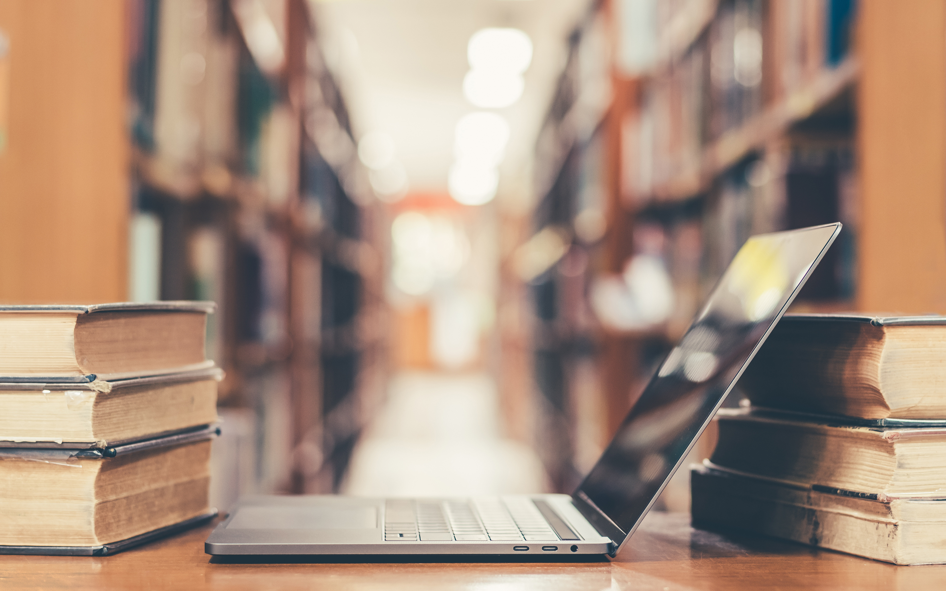 An open laptop in a library, surrounded by old bookshelves