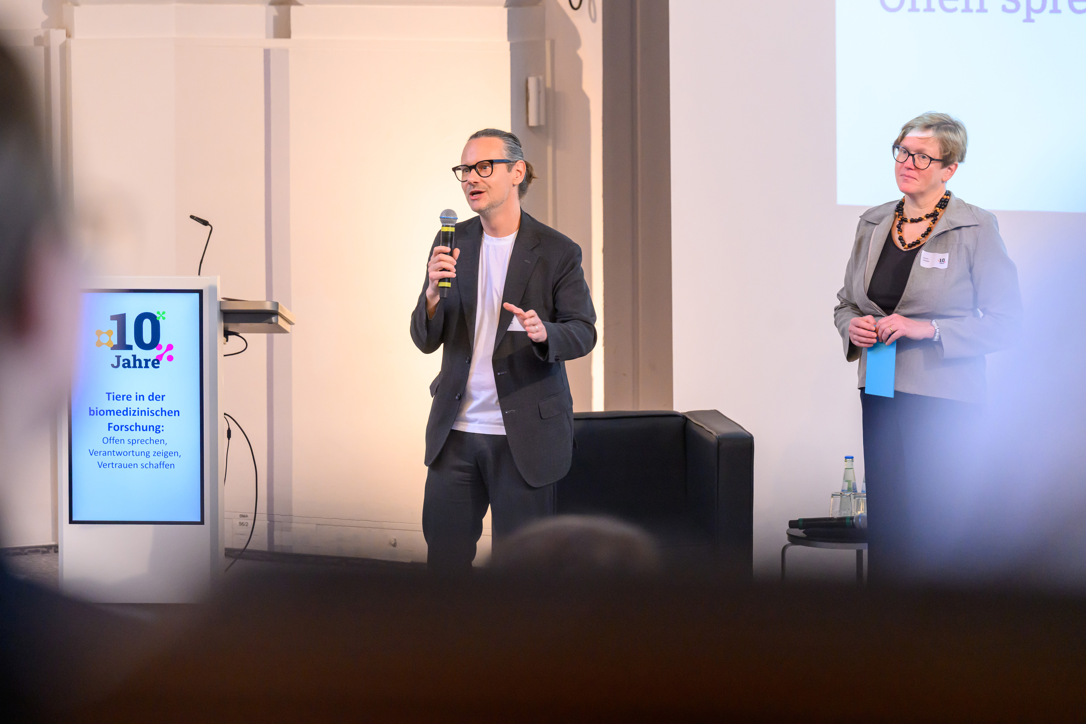 Andreas Scheu steht mit einem Mikrofon in der Hand auf der Bühne und beantwortet eine Frage